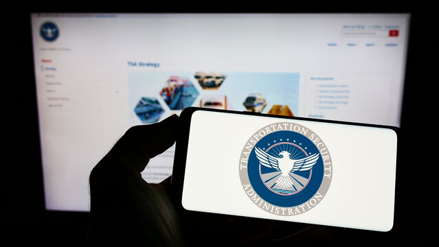 Stuttgart, Germany - 10-24-2022: Person holding cellphone with seal of Transportation Security Administration (TSA) on screen in front of business webpage. Focus on phone display.