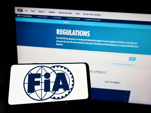 Stuttgart, Germany - 10-24-2022: Person holding mobile phone with logo of International Automobile Federation (FIA) on screen in front of web page. Focus on phone display.