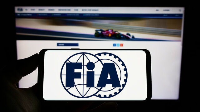 Stuttgart, Germany - 10-24-2022: Person holding cellphone with logo of International Automobile Federation (FIA) on screen in front of webpage. Focus on phone display.