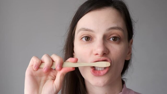 Smiling brunette woman with organic bamboo toothbrush and toothpasteis brushing her white teeth. Biodegradable ecological personal care products. Plastic free lifestyle concept.