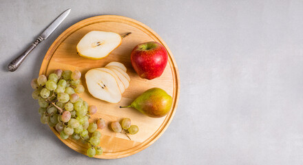 Autumn fruits. Pear, apple and grapes on a round wooden cutting board.