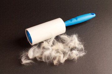 Cloth fabrics cleaner lint roller brush with paper roll blue grip and cat fur on black color background. sticky roller, pet cat dog fur dust hair remover. Close-up