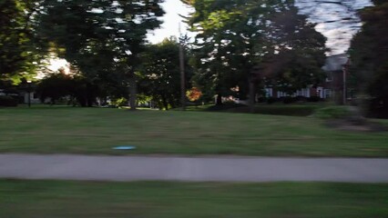 Car passenger point of view looking out window driving by Midwest middle class suburb neighborhood near downtown Columbus, Ohio during a sunny evening