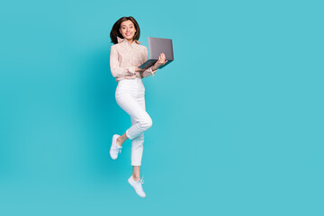 Fototapeta na wymiar Full length photo of young carefree pretty business lady jumping air trampoline hold netbook empty space ad new job freelancer isolated on blue color background