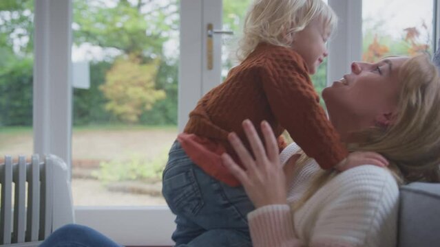 Mother and son sitting on floor next to portable plug in radiator playing game and trying to keep warm during energy crisis - shot in slow motion