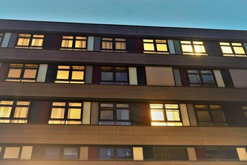 Krankenhausgebäude mit goldgelbem Licht in Fenstern vor blauem Himmel am frühen Morgen im Herbst