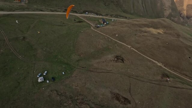 Aerial view orange paraglider flying extreme sport activity mountain rocky terrain valley enjoy freedom. FPV drone shot paraplane parachute outdoor adventure over cliff summit sky countryside scenery
