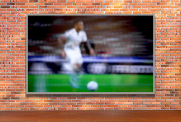 TV with soccer player on brick wall and wooden table with empty space. Selective focus. Blurred background.
