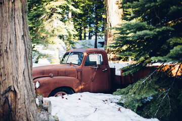 Old rusty red car in the snow and pines, great for vintage vibes cozy Christmas style shoots