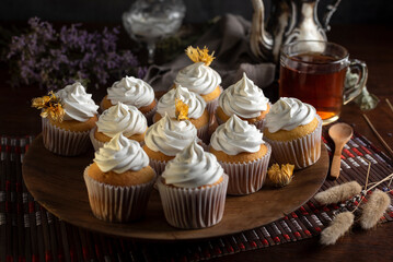 muffins or madeleines on a can and a wooden board with meringue and cream on top with an old teapot cup of tea and decorated with natural flowers