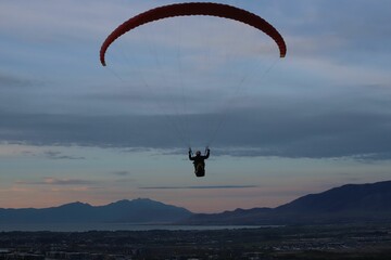 Person paragliding on the background of mountainous landscape at late sunset