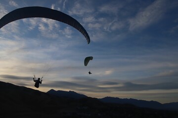Silhouettes of people paragliding on the mountainous background under the cloudy sky