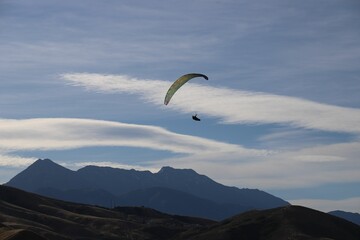 Person paragliding on the background of mountainous landscape under the cloudy sky
