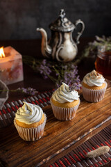 muffins or madeleines on a can and a wooden board with meringue and cream on top with an old teapot cup of tea and decorated with natural flowers