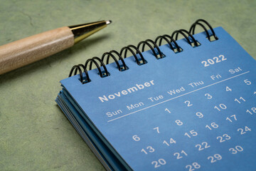 November 2022 - small spiral desktop calendar with a stylish pen against textured  paper,  time and business concept