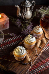 Obraz na płótnie Canvas muffins or madeleines on a can and a wooden board with meringue and cream on top with an old teapot cup of tea and decorated with natural flowers