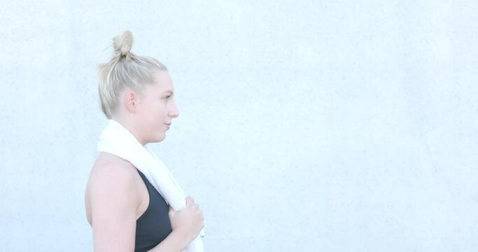 Portrait of an attractive sexy and vivacious young caucasian blonde sporty woman in sports clothing with towel around neck resting after a workout. High quality 4k footage