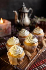 muffins or madeleines on a can and a wooden board with meringue and cream on top with an old teapot cup of tea and decorated with natural flowers