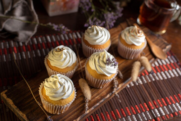 muffins or madeleines on a can and a wooden board with meringue and cream on top with an old teapot cup of tea and decorated with natural flowers