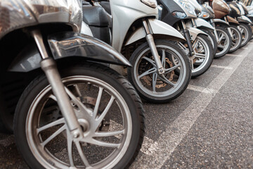 Motorcycles and mopeds are parked in the parking lot. Bike wheels with tires in the city of Italy