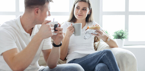 young couple drinks coffee sitting on the sofa in a new apartment.