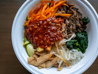 Korean Bibimbap, rice bowl with beef, vegetables, and hot pepper jelly sauce including spinach, carrot, radish, cucumber, bean sprouts, and garlic