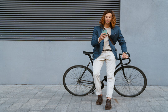 Ginger man using mobile phone while walking with bicycle on city street