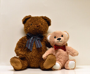 stuffed Brown an tan bears sitting side by side with a paw around each other with a red bow tie and a plaid bow tie