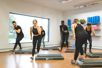 Diverse group of fit people in sportswear doing stretching and fitness exercise together on a the floor of a gym during an exercise session