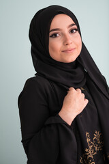 beautiful muslim woman in fashinable dress with hijab isolated on modern cyan background representing concept of modern islam and ramadan kareem