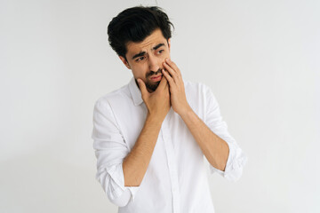 Studio portrait of sick man suffering from dental pain, touching painful cheek and grimacing on...