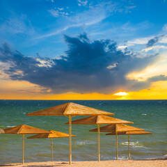 sandy sea beach with sun umbrella at the sunset