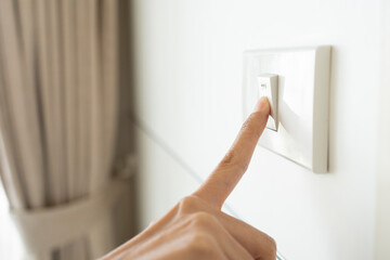 close up hand of woman turning off light switch in a home.