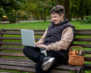 Obraz premium Young man sitting on bench with laptop in the park