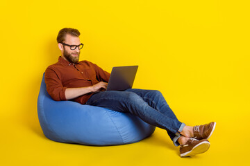 Full length portrait of handsome smart guy sit cozy bag use netbook isolated on yellow color background