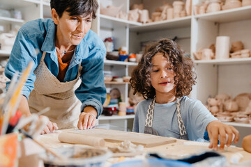 Mature woman teaching boy to make clay crafts in pottery workshop - obrazy, fototapety, plakaty