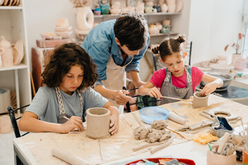 Mature female teacher working with group of kids in pottery workshop