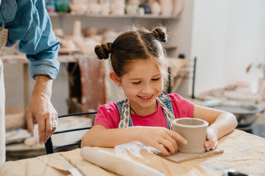 Cute girl smiling and sculpting while sitting at the table in ceramics class