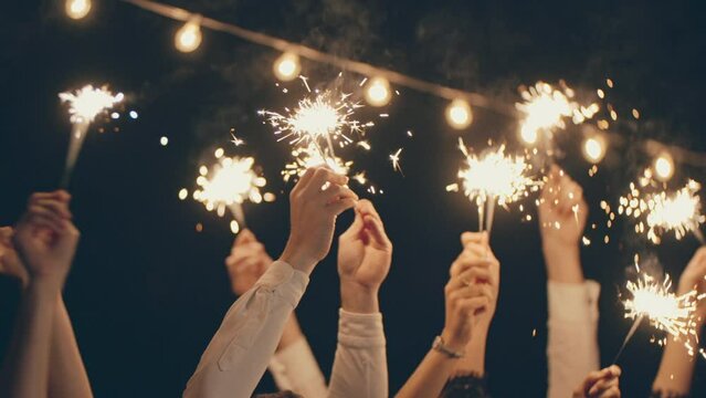Group of hands holding sparklers in the air at night xmas outdoors. Christmas party, new year holiday and vacation. Young people celebrate together, enjoying, dance and laugh. Festive mood