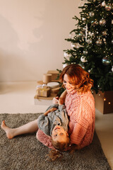 A little daughter, a child and a pregnant mother in knitted sweaters cuddle spend time together in the decorated interior of a Scandinavian-style room on a Christmas holiday at home. Selective focus
