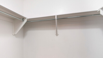 Panorama White shelves with wooden brackets and metal rods inside a walk in closet