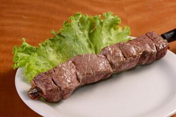 Fototapeta premium Meat barbecue on skewers. Traditional Brazilian kebab in white plate on wooden table.
