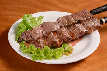 Meat barbecue on skewers. Traditional Brazilian kebab in white plate on wooden table.