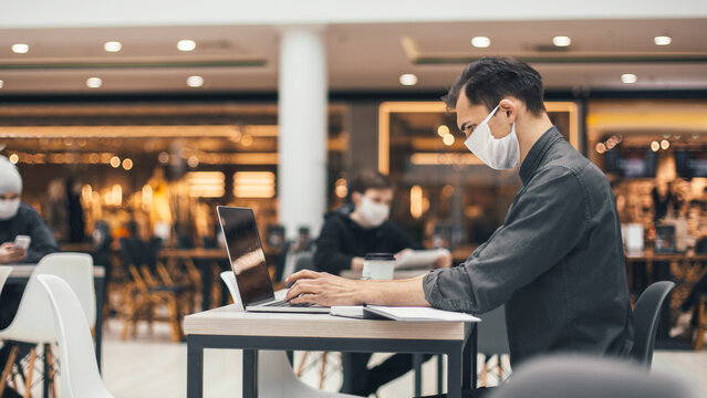 image of people in protective masks using laptops in a food court.