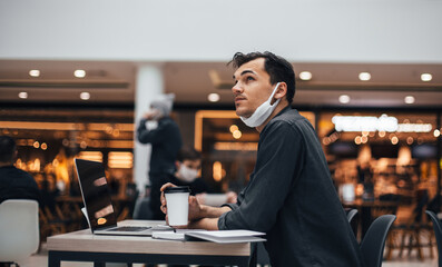 young man with a coffee takeaway sitting at a cafe table