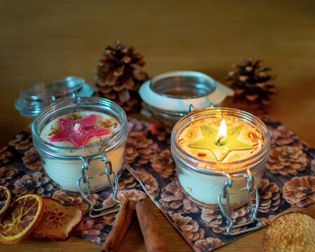 Zwei weihnachtliche Kerzen, eine brennend, in Einmachgläsern mit Bügelverschluss.