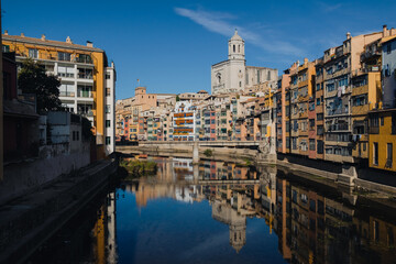 Fototapeta na wymiar Girona, Spain on 22 October 2022: Colorful yellow and orange houses in historical jewish quarter of Girona, Catalonia, Spain reflecting on the Oñar river with clear blue sky