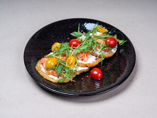Close-up of fresh potato pancakes with arugula, cherry tomatoes and salmon on a beautiful black plate. Delicious food in the restaurant.