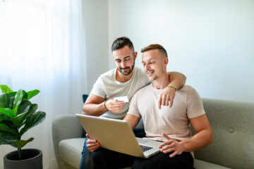 Happy young two man couple using laptop computer while sitting on a couch at home