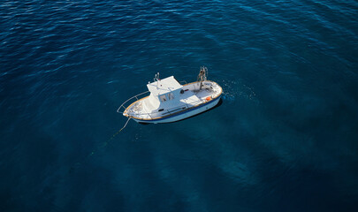 Aerial view of a little fishing boat at dawn surrounded by a crystalline deep blue sea moored in Calabria, Italy.